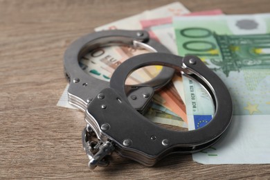 Photo of Corruption. Handcuffs and euro banknotes on wooden table, closeup