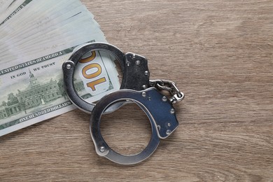 Photo of Corruption. Handcuffs and dollar banknotes on wooden table, flat lay