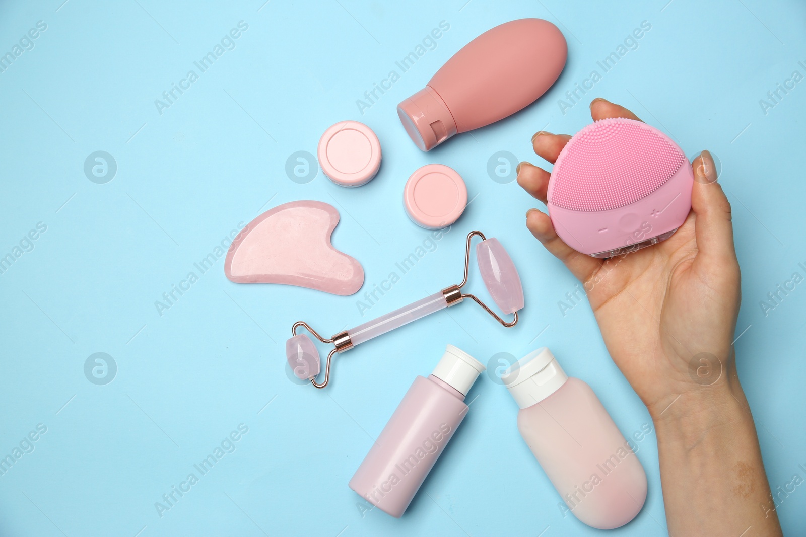 Photo of Woman holding facial cleansing brush near other skin care products on light blue background, top view. Space for text