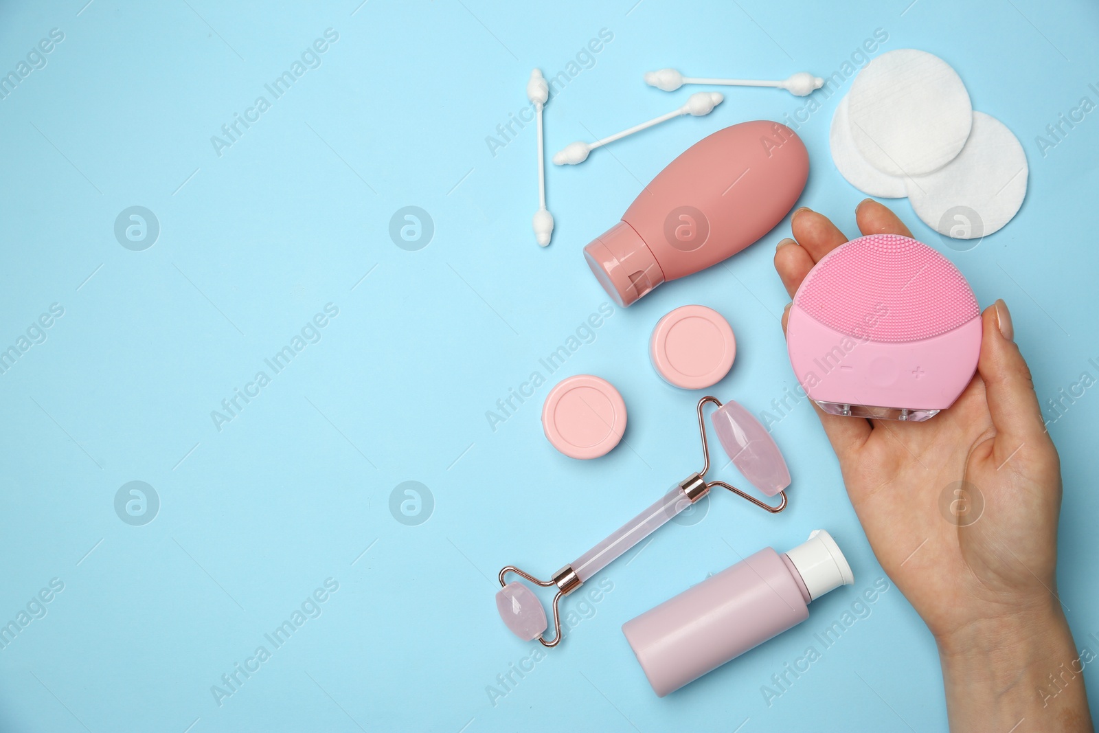 Photo of Woman holding facial cleansing brush near other skin care products on light blue background, top view. Space for text