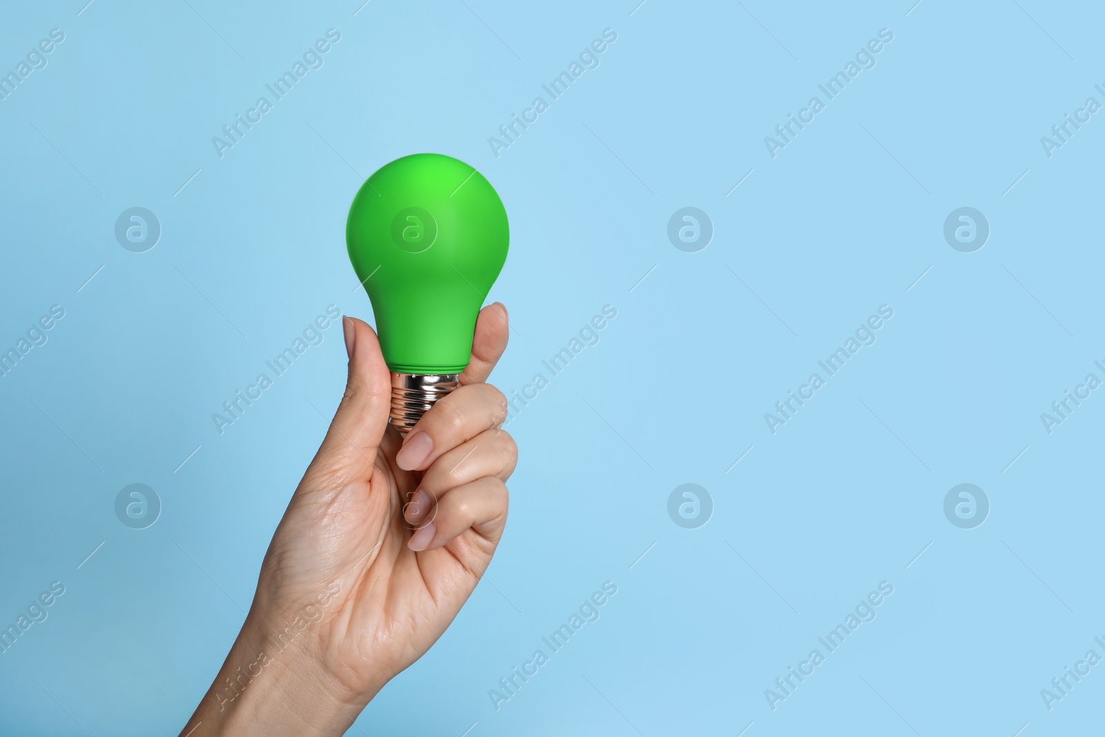 Image of Woman holding green bulb on light blue background, closeup. Space for text