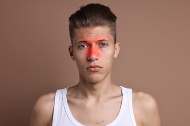 Young man suffering from sinusitis on light brown background