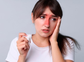 Woman with tissue suffering from sinusitis on light blue background