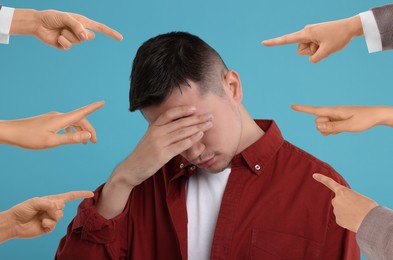 People pointing at embarrassed man on light blue background