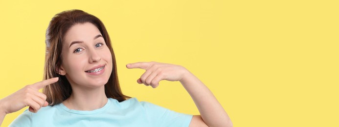 Image of Beautiful woman with braces pointing at her mouth on yellow background. Banner design with space for text