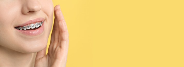 Woman with braces smiling on yellow background, closeup. Banner design with space for text