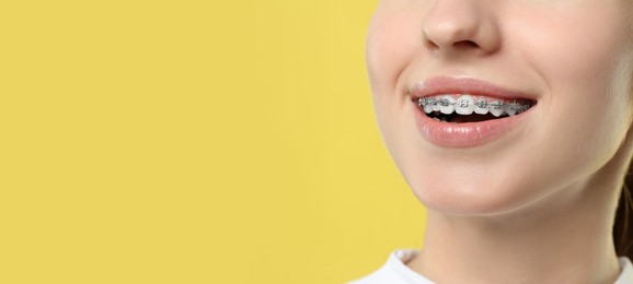 Woman with braces smiling on yellow background, closeup. Banner design with space for text