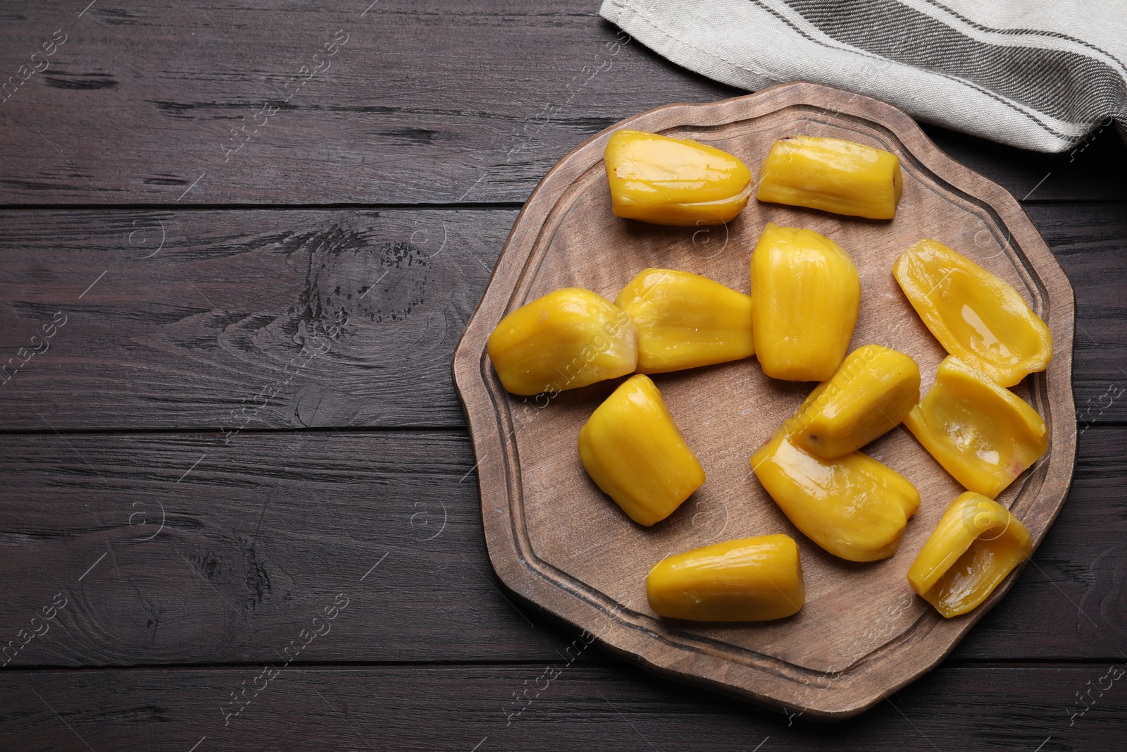 Photo of Fresh exotic jackfruit bulbs on black wooden table, flat lay. Space for text