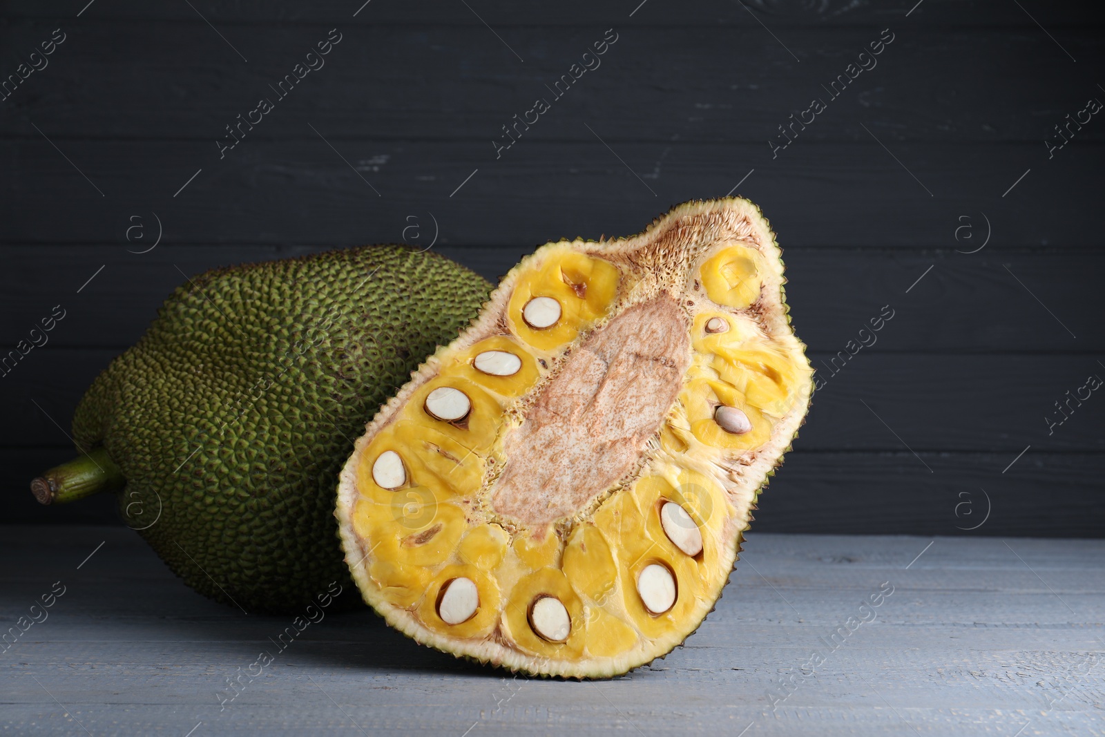 Photo of Delicious cut and whole exotic jackfruit on grey wooden table