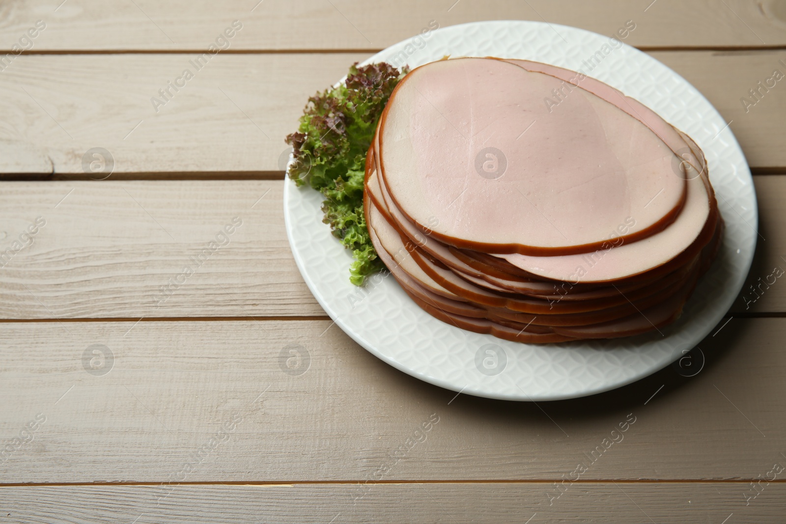 Photo of Slices of delicious boiled sausage with lettuce on beige wooden table, space for text