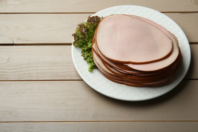 Slices of delicious boiled sausage with lettuce on beige wooden table, space for text