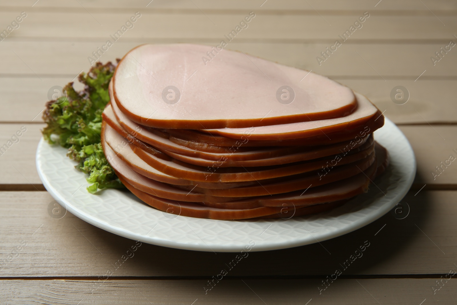 Photo of Slices of delicious boiled sausage with lettuce on beige wooden table, closeup