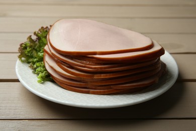 Slices of delicious boiled sausage with lettuce on beige wooden table, closeup