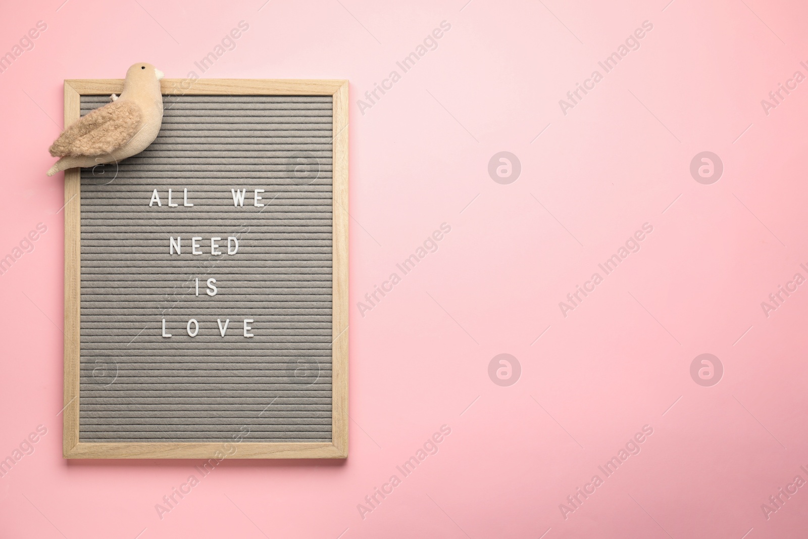 Photo of Letter board with phrase All We Need Is Love and bird figure on pink background, top view. Space for text