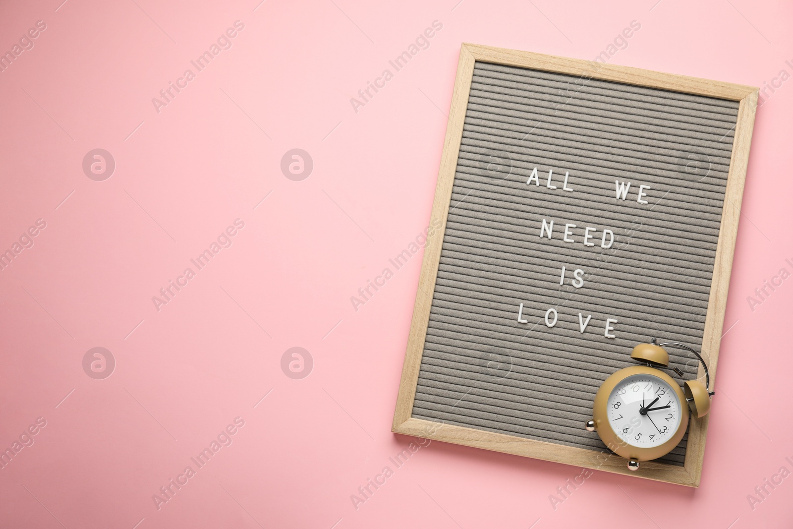 Photo of Letter board with phrase All We Need Is Love and alarm clock on pink background, top view. Space for text