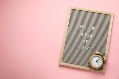 Photo of Letter board with phrase All We Need Is Love and alarm clock on pink background, top view. Space for text