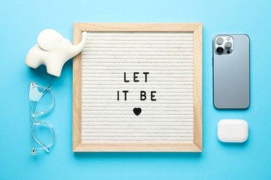 Photo of Letter board with phrase Let It Be, smartphone, glasses, elephant figure and earphones on light blue background, flat lay