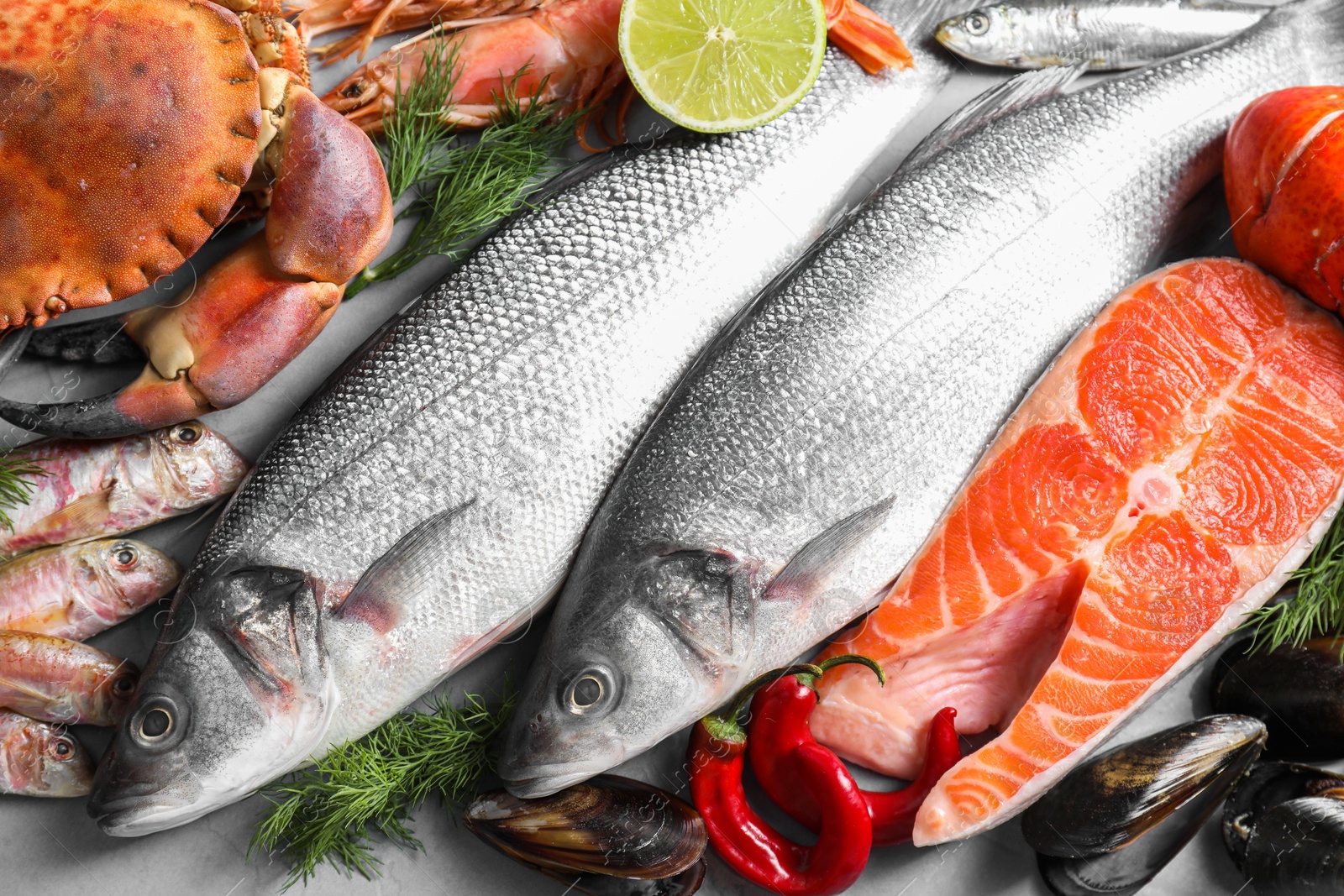 Photo of Many different sea food, lime and dill on grey table, flat lay