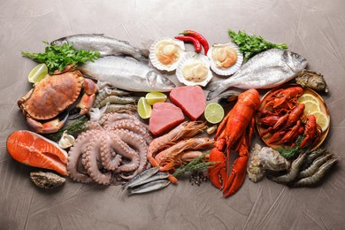 Photo of Many different sea food, herbs and lime on grey textured table, flat lay