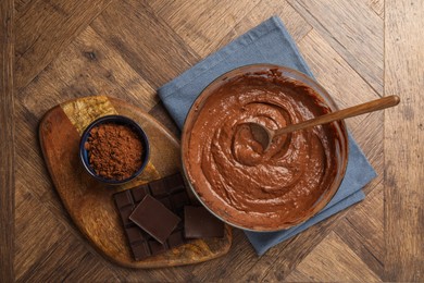 Photo of Chocolate dough in bowl, spoon and ingredients on wooden table, flat lay