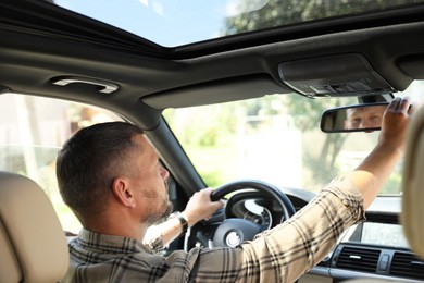 Photo of Man adjusting rear view mirror while driving car