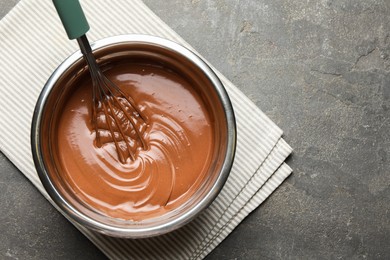 Photo of Chocolate dough and whisk in bowl on grey table, top view. Space for text