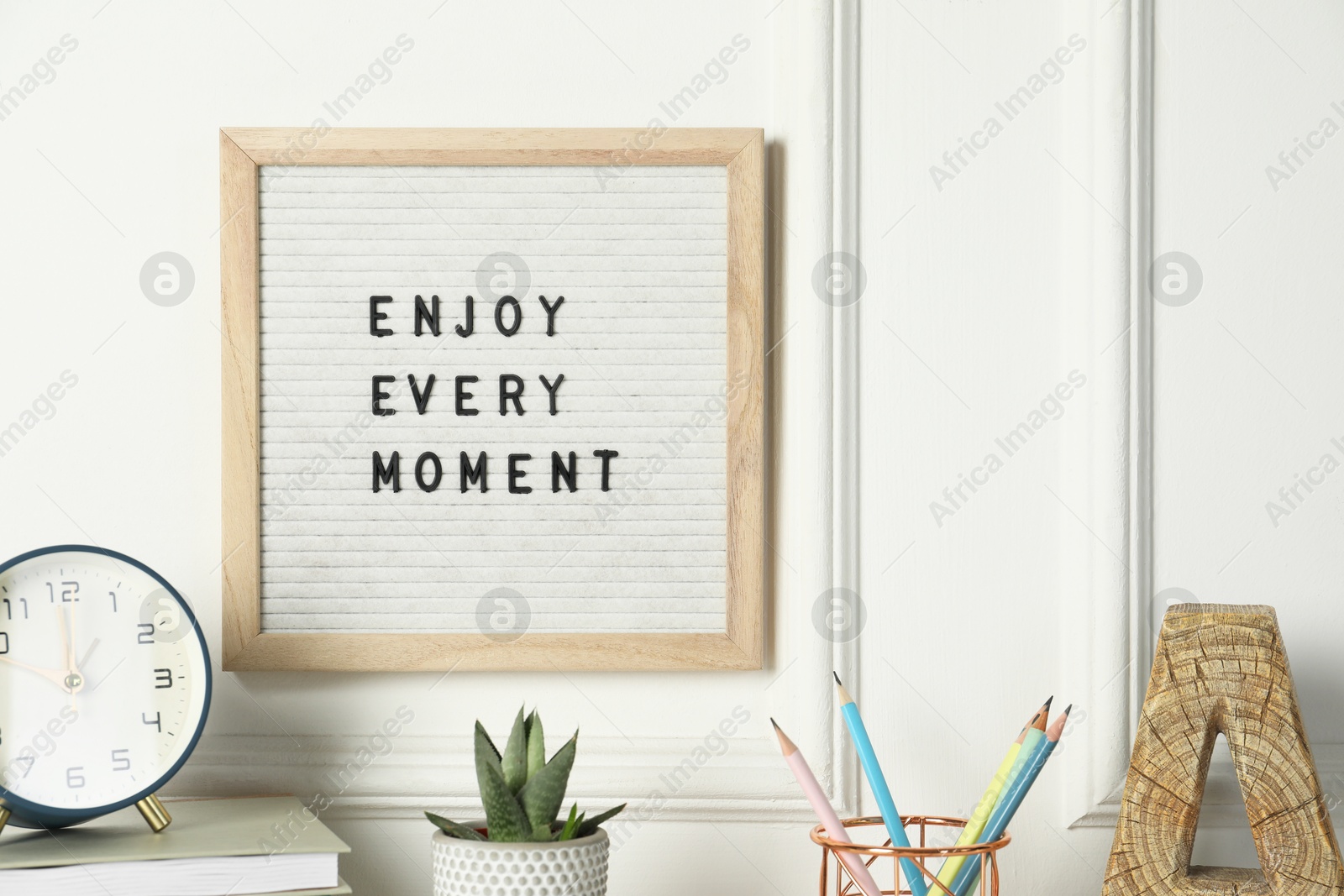 Photo of Letter board with phrase Enjoy Every Moment, alarm clock, decor and stationery on white desk