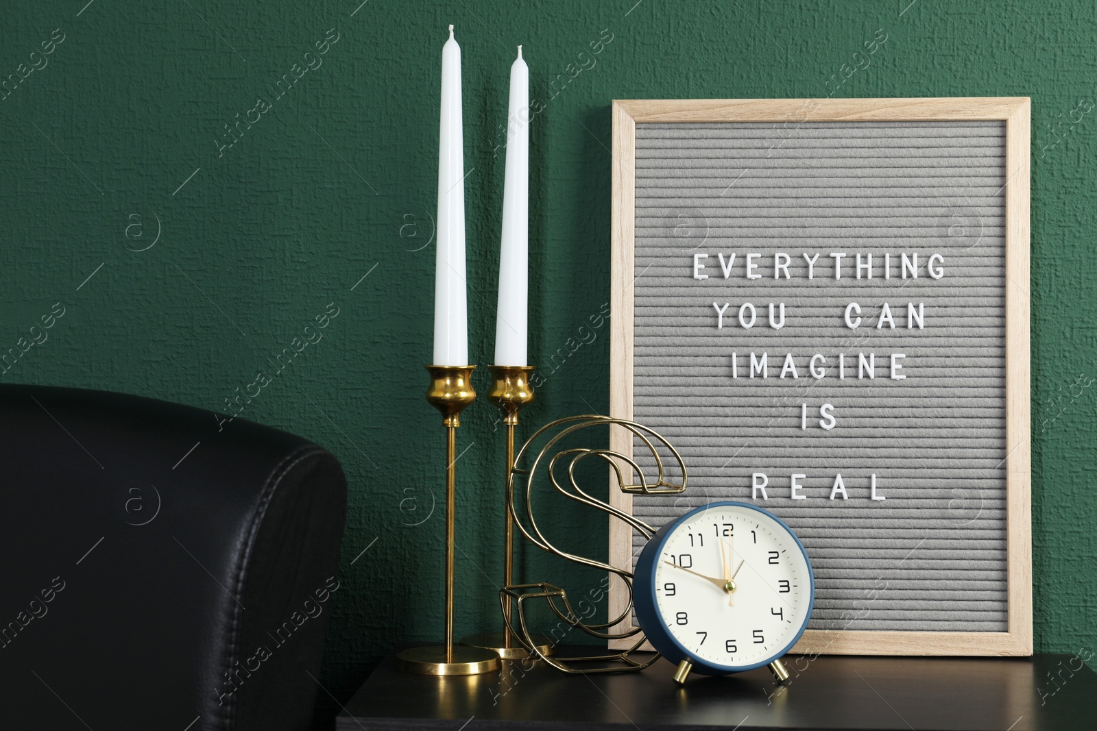 Photo of Letter board with phrase Everything You Can Imagine Is Real, alarm clock, candles and decor element on table near green wall