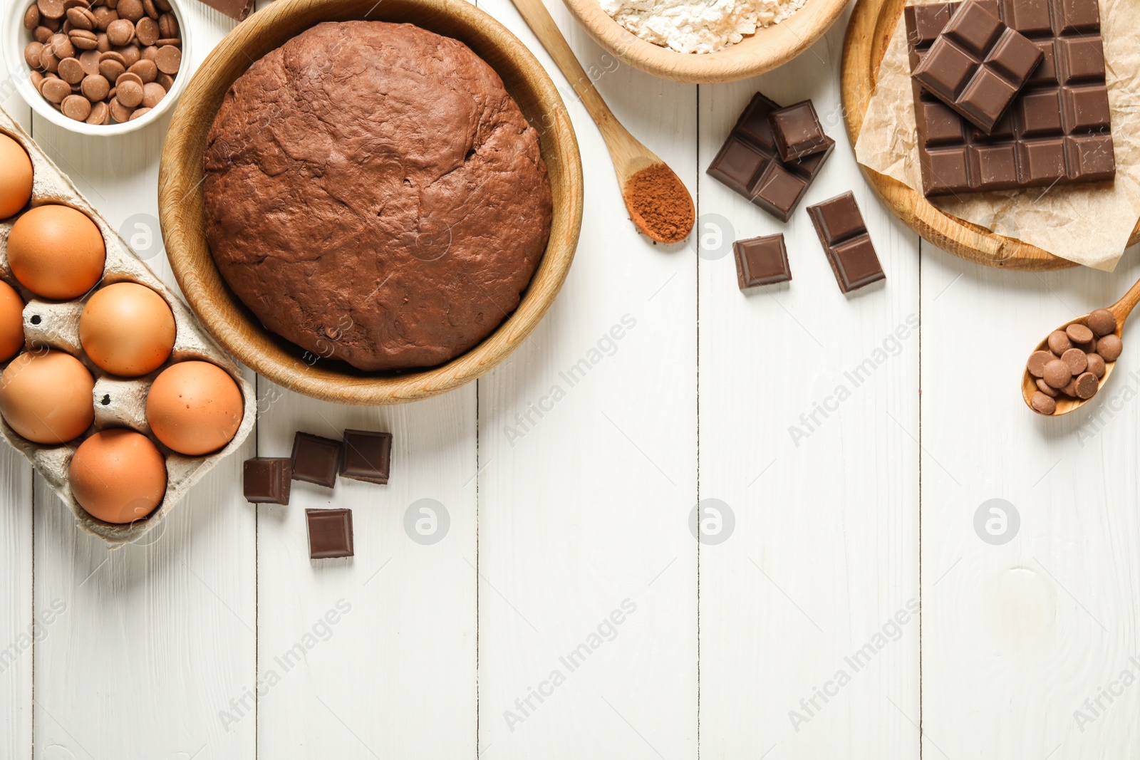 Photo of Chocolate dough and ingredients on white wooden table, flat lay. Space for text