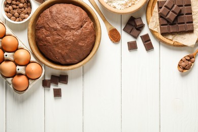 Photo of Chocolate dough and ingredients on white wooden table, flat lay. Space for text