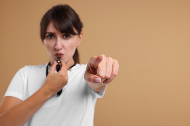 Woman blowing whistle on beige background, selective focus. Space for text