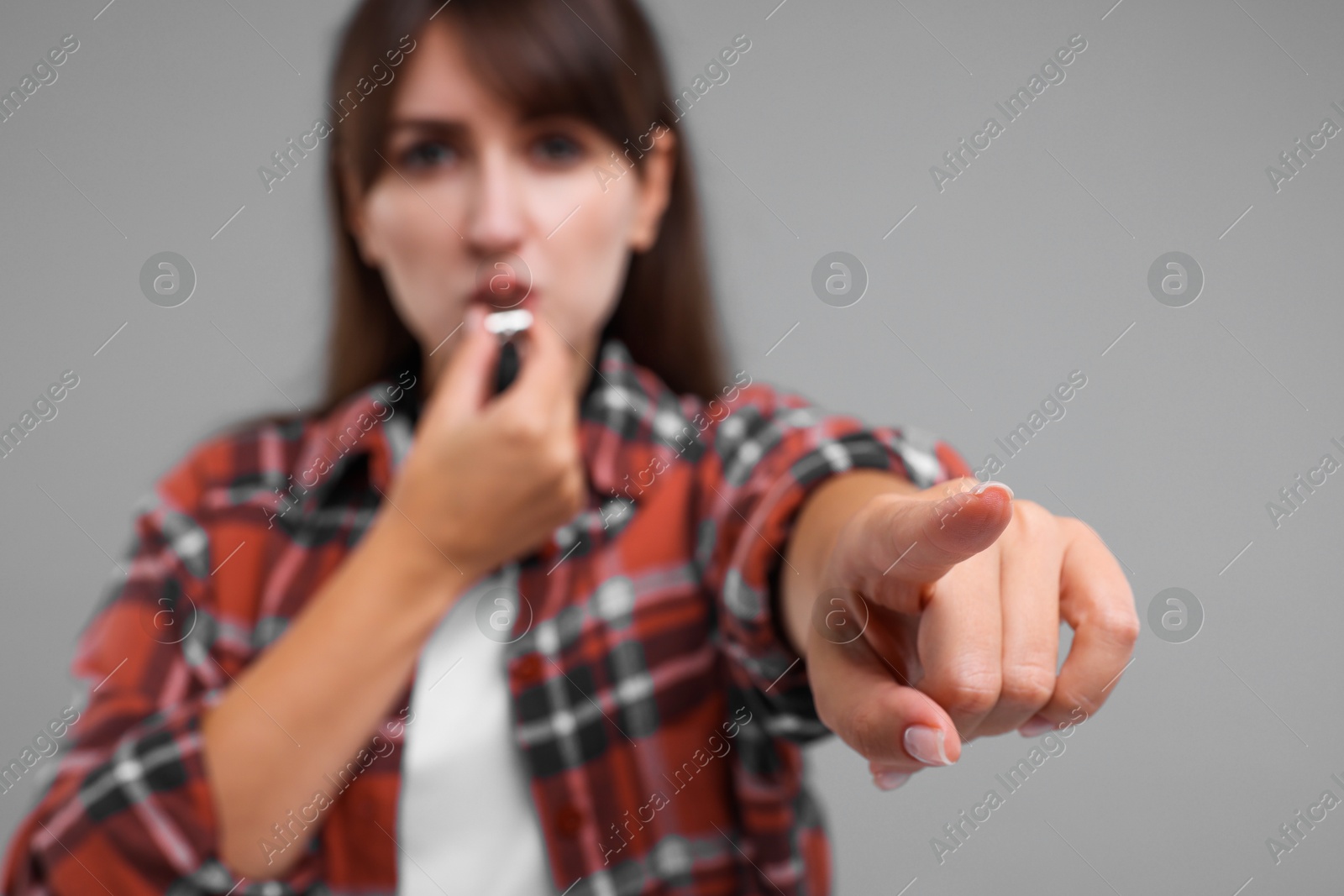 Photo of Woman blowing whistle on grey background, selective focus