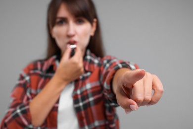 Woman blowing whistle on grey background, selective focus