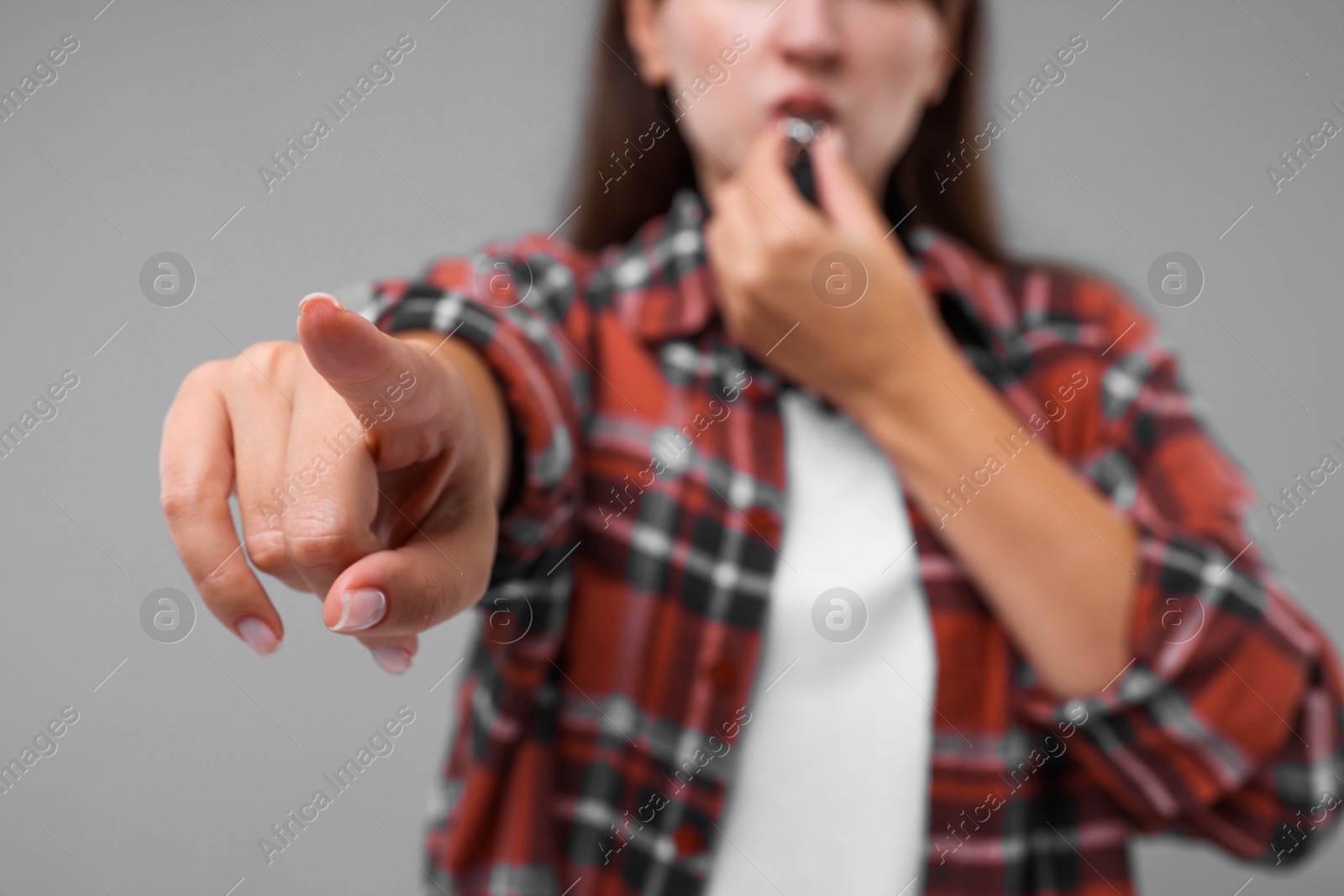 Photo of Woman blowing whistle on grey background, closeup