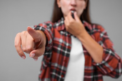 Woman blowing whistle on grey background, closeup