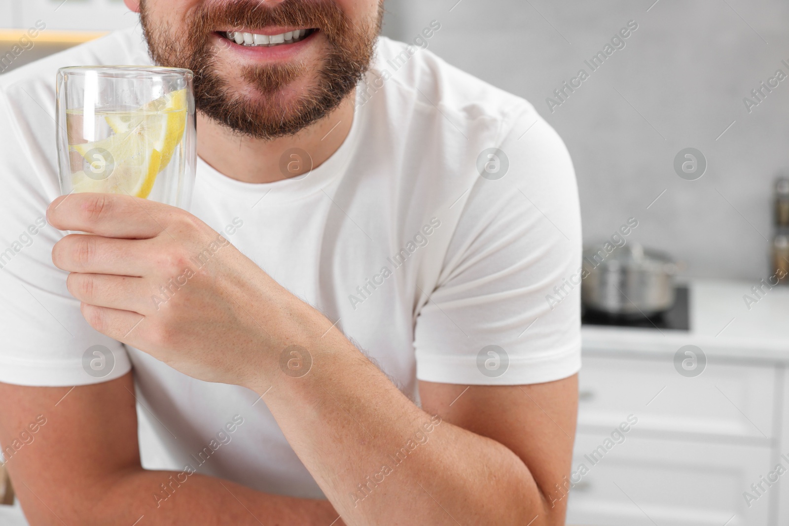 Photo of Happy man holding glass of water with lemon in kitchen, closeup