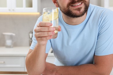 Happy man holding glass of water with lemon indoors, closeup