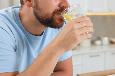 Photo of Man drinking water with lemon indoors, closeup