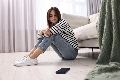 Loneliness concept. Sad teenage girl with smartphone on floor at home