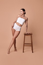 Photo of Smiling woman with perfect skin in underwear posing with stool against beige background. Body care