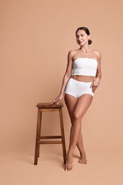 Photo of Smiling woman with perfect skin in underwear posing with stool against beige background. Body care