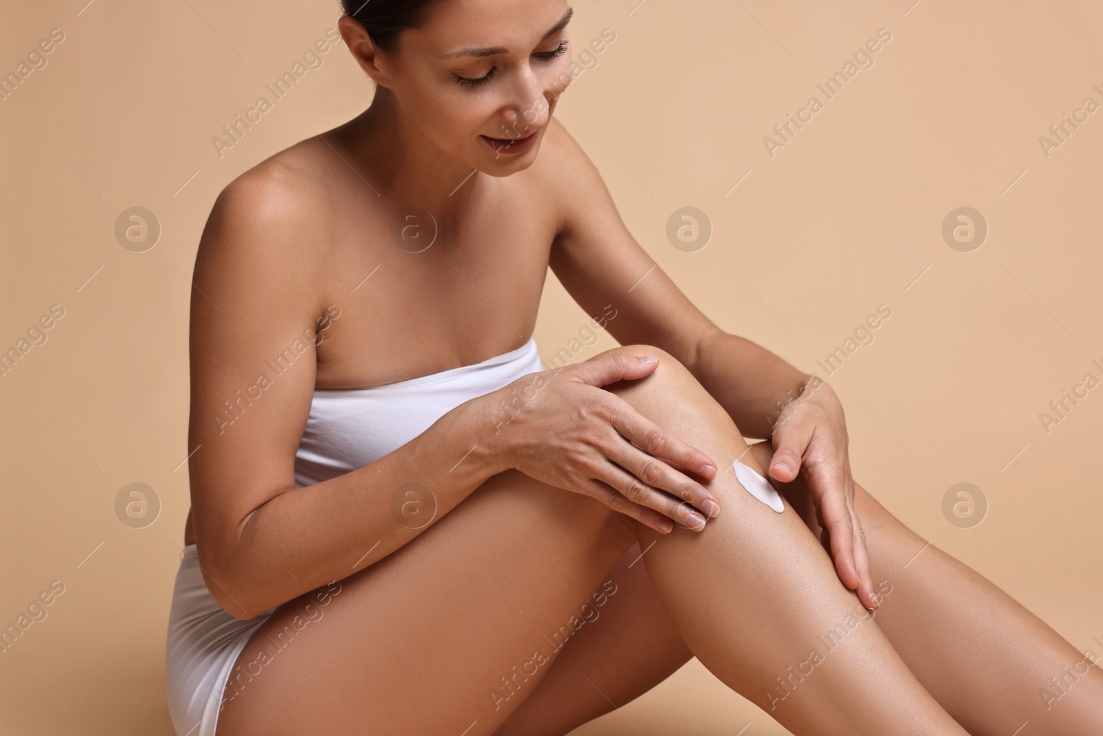 Photo of Beautiful woman applying cream onto leg against beige background. Body care