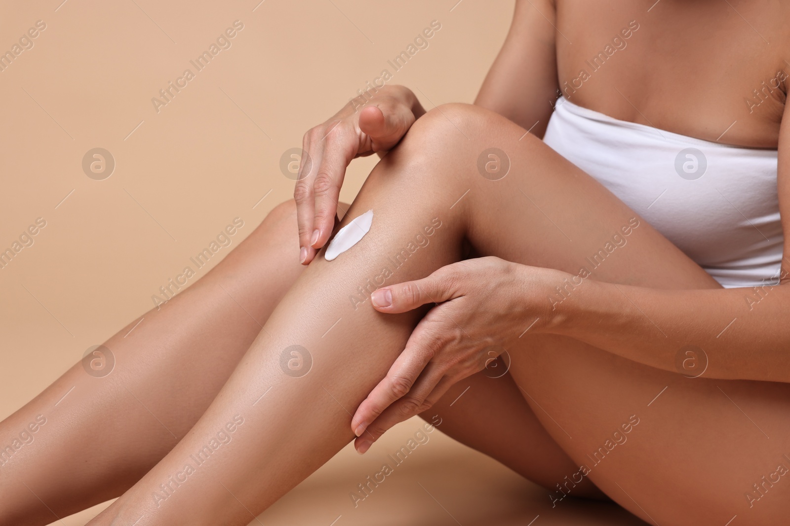 Photo of Woman applying cream onto leg against beige background, closeup. Body care