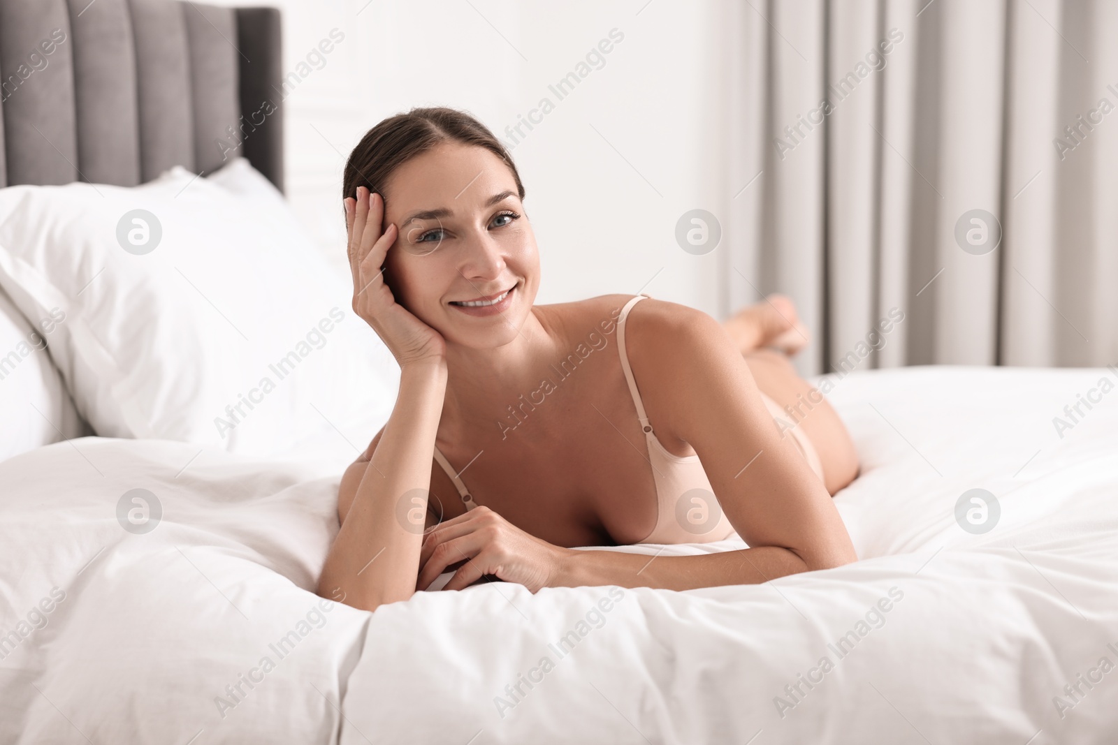 Photo of Smiling woman with perfect skin posing on bed. Body care