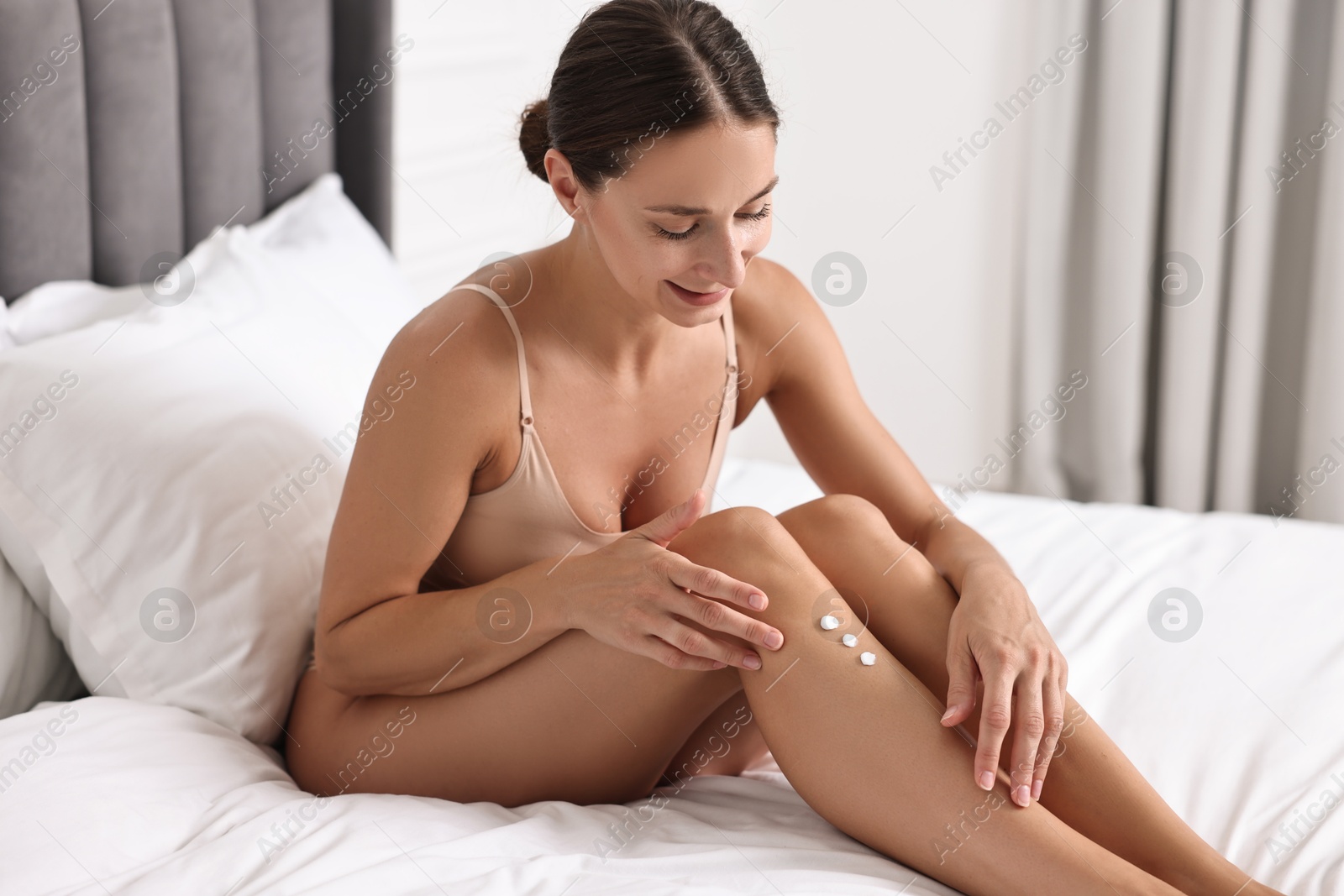 Photo of Beautiful woman applying cream onto leg on bed. Body care