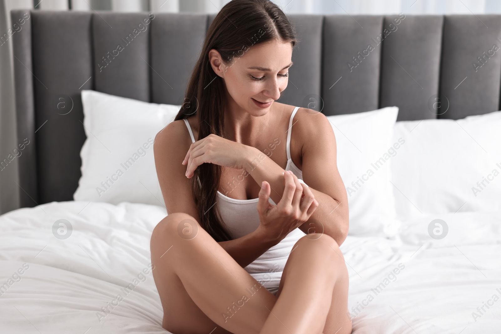 Photo of Beautiful woman with perfect skin applying cream onto hand on bed. Body care