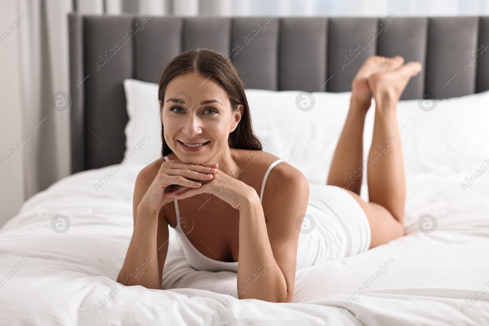 Photo of Smiling woman with perfect skin posing on bed. Body care