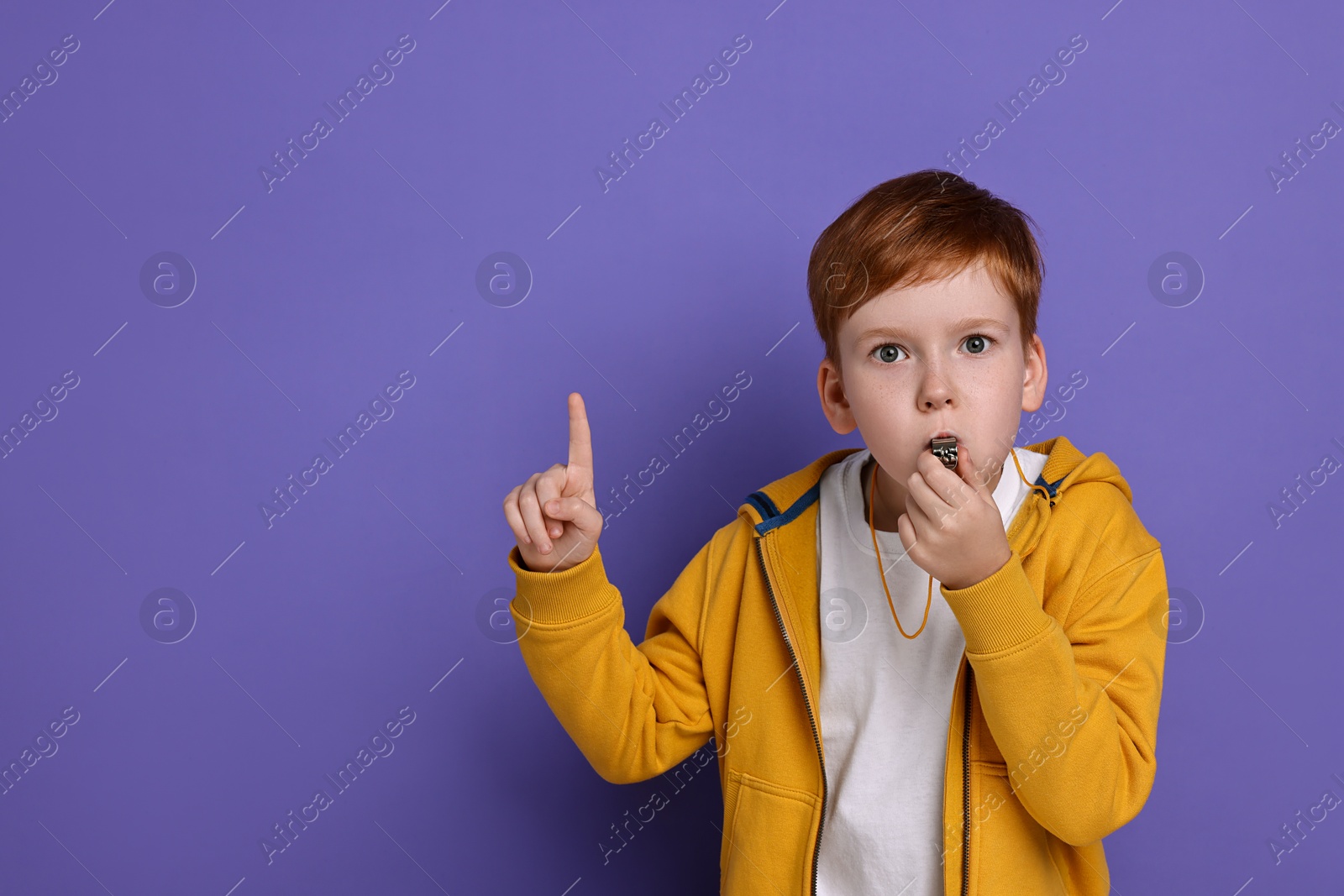 Photo of Little boy blowing whistle on purple background, space for text