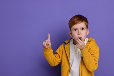 Photo of Little boy blowing whistle on purple background, space for text