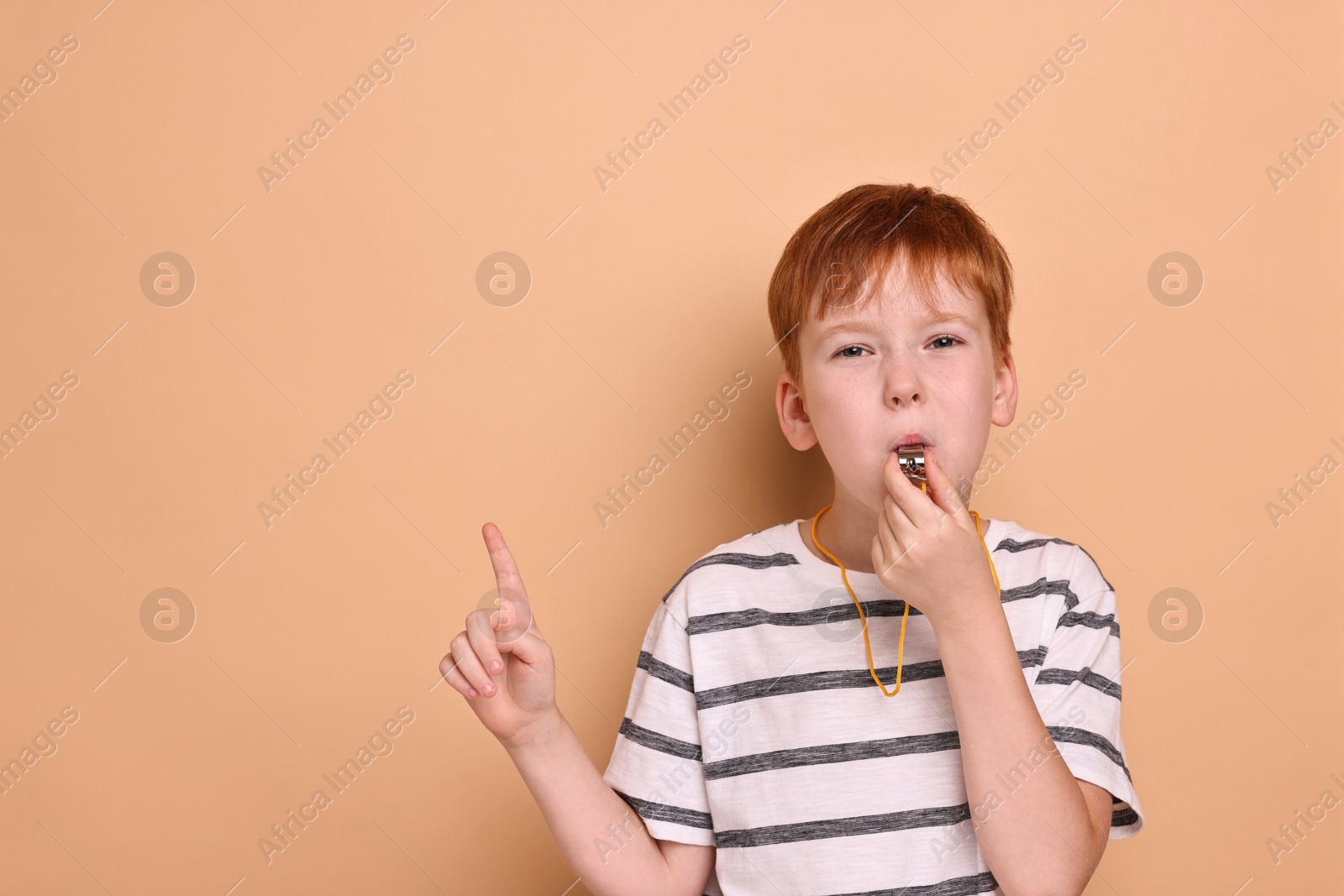 Photo of Little boy blowing whistle on beige background, space for text